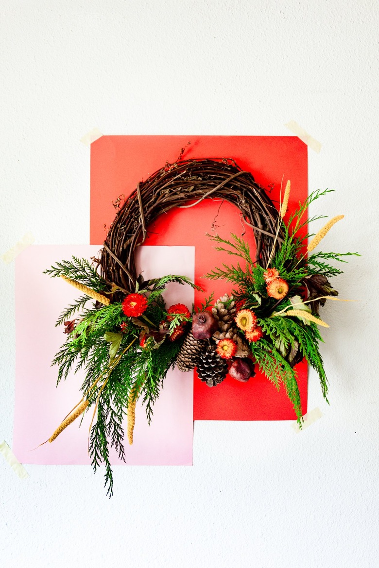 a holiday wreath made with cedar branches, pine cones, dried flowers, and dried pomegranates