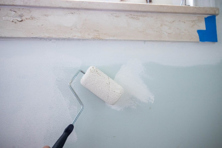 Paint roller with white paint, painting over a light blue wall