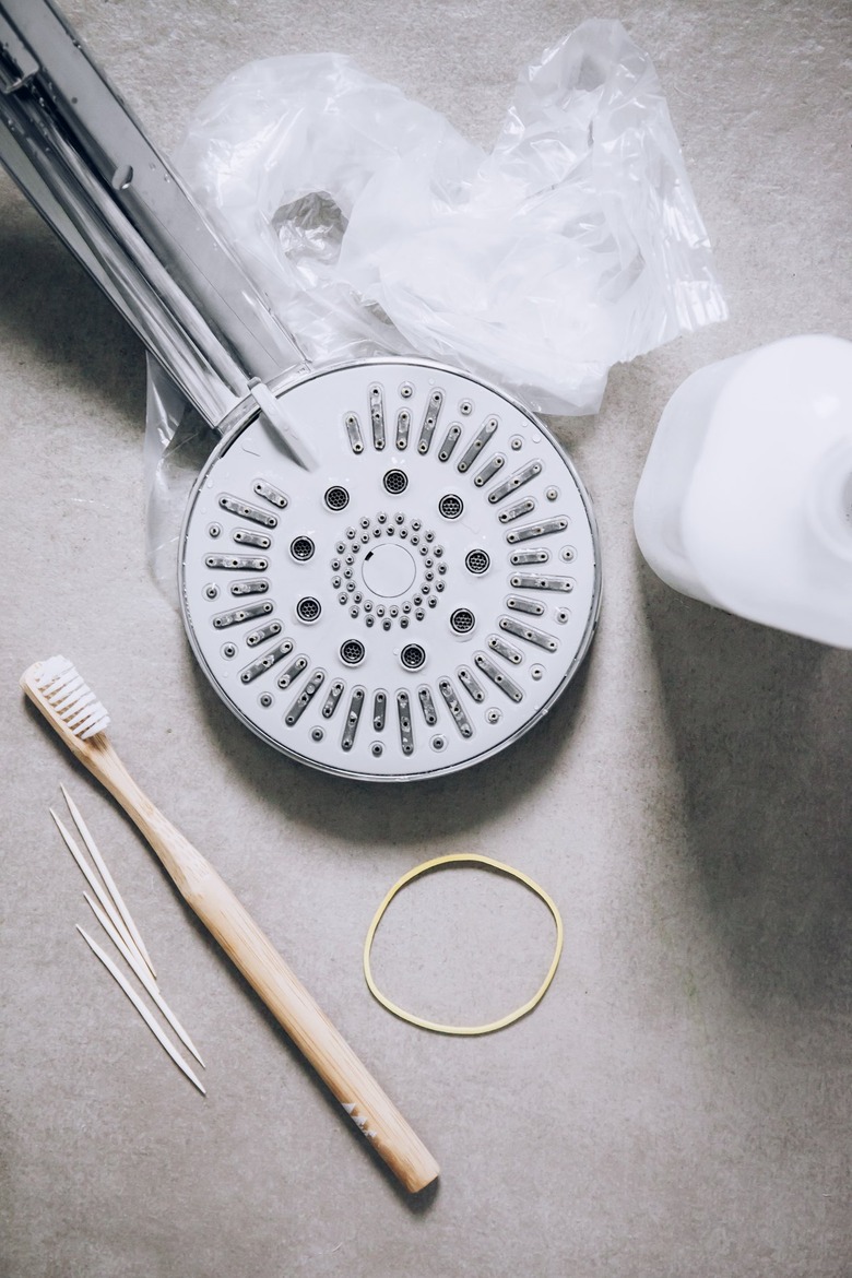 Silver shower head, toothbrush, tooth pics, plastic bag, rubber band, and plastic jug on concrete flooring