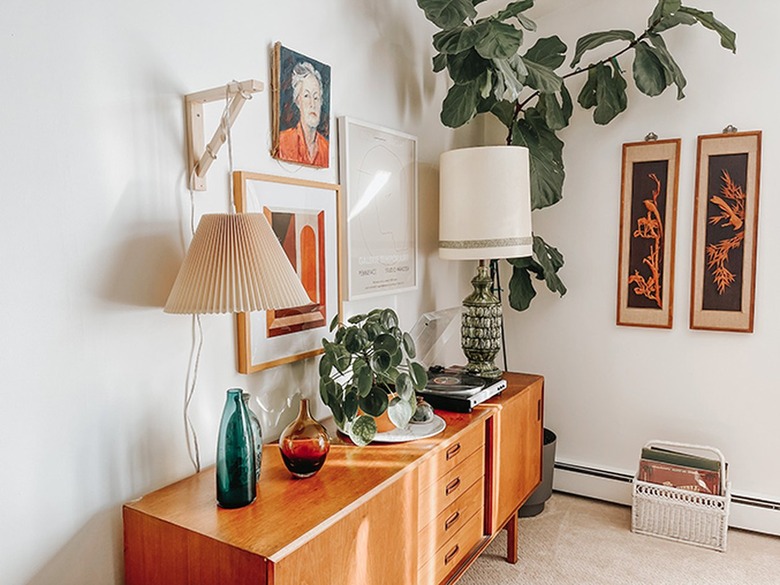 Beige pleated lampshade on a wood bracket, eclectic art, plant, vintage accents, record player, and wood sideboard