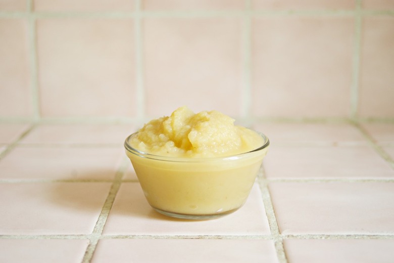 A clear bowl full of applesauce on a white tile surface.