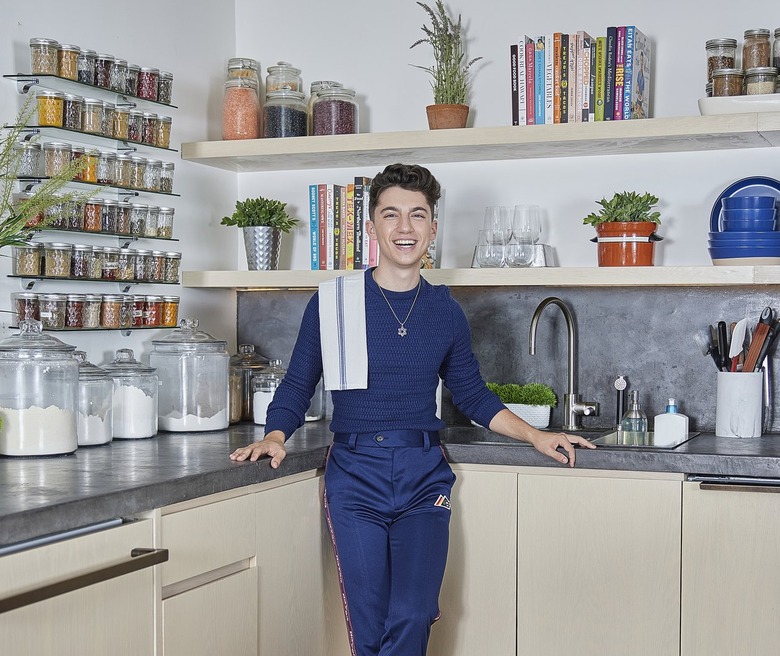 Eitan Bernath wearing all blue with a white towel thrown over his shoulder in his kitchen in Manhattan.