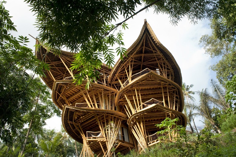 A large bamboo building with two structures in the woods.