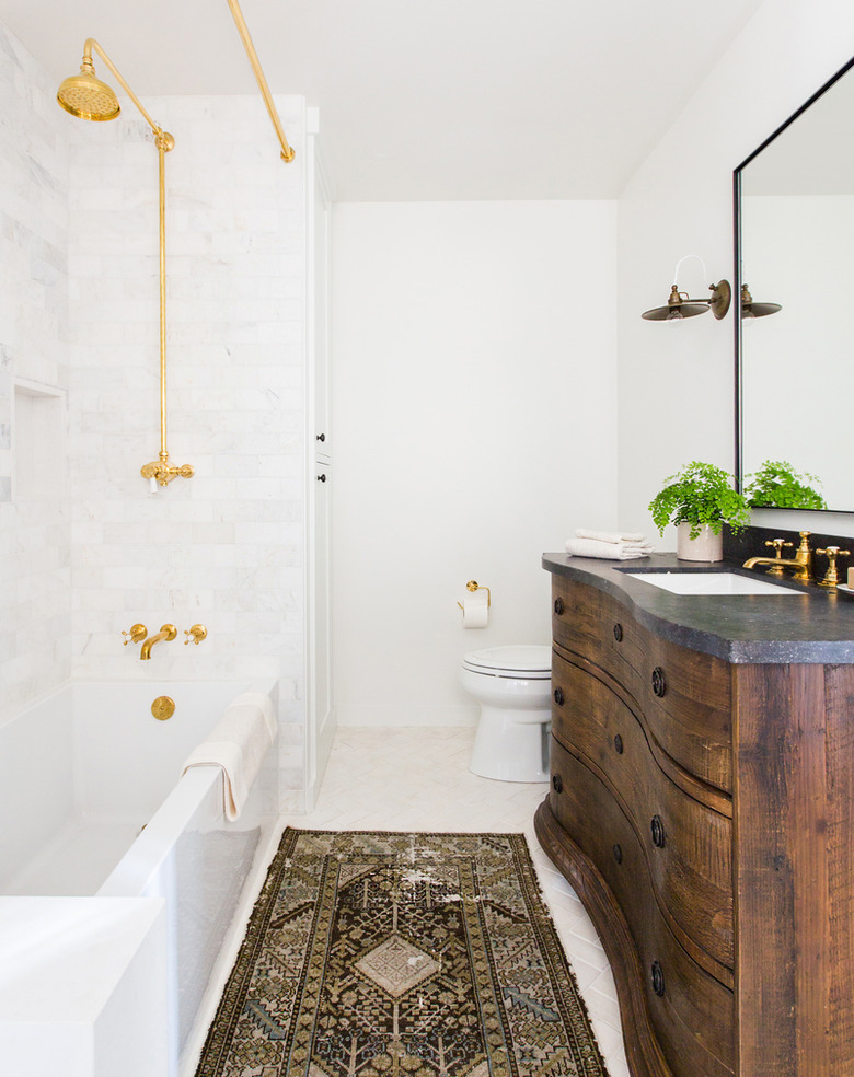 Bathroom with white tub, brass fixtures, antique vanity.