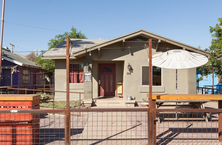 light green house with patio table and umbrella in front yard, string lights, and fence