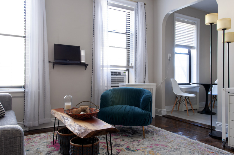 living room with white curtains, wooden table, and blue velvet chair