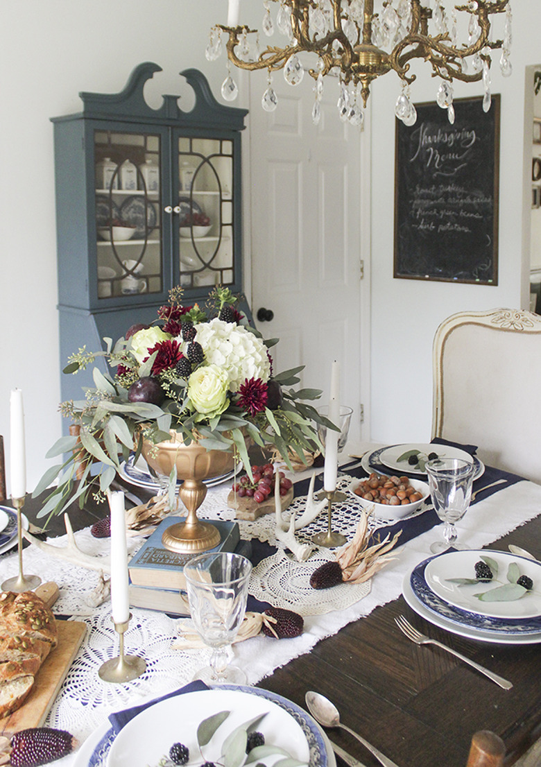 Jewel tone fall centerpiece with burgundy flowers and greenery in farmhouse dining room