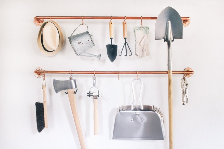 garage tools hanging on s-hooks that are suspended from copper pipes mounted on a wall