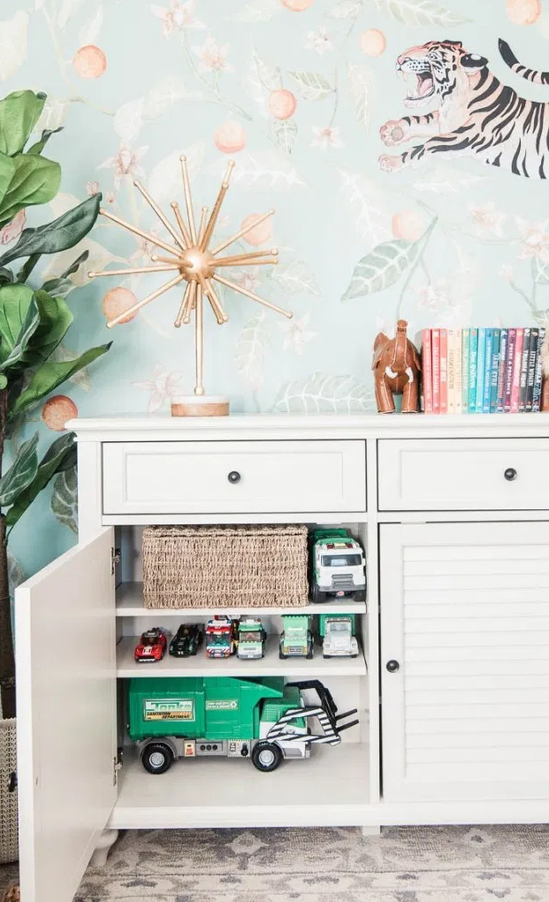 Family room toy storage in white cabinet storing trucks and other toys