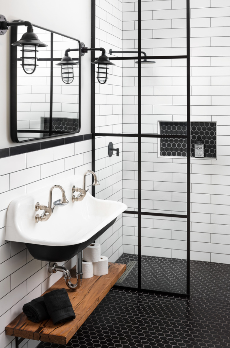 farmhouse bathroom lighting with cage style wall sconces mounted to white shiplap walls with black mosaic penny tile and trough sink