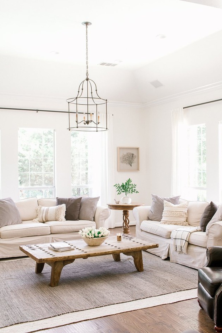 Farmhouse living room with two couches, pillows, chandelier, coffee table, rug.