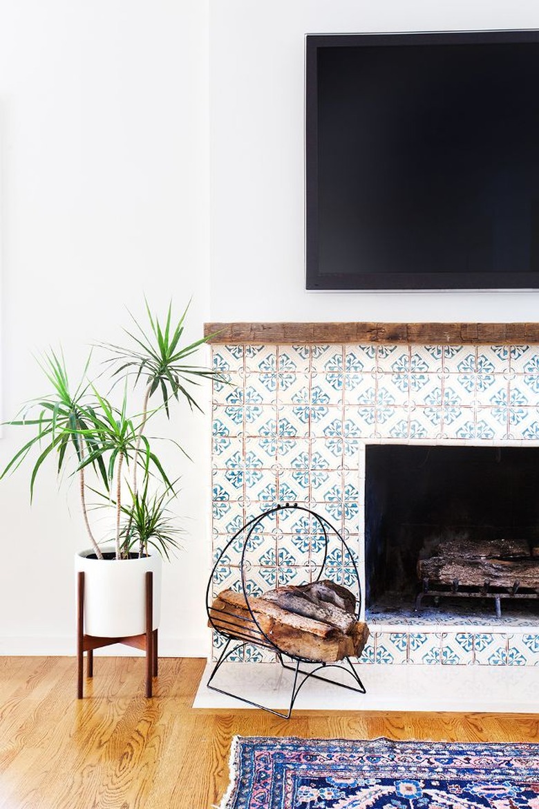 Fireplace with tile, flat screen , plant, logs and rug.