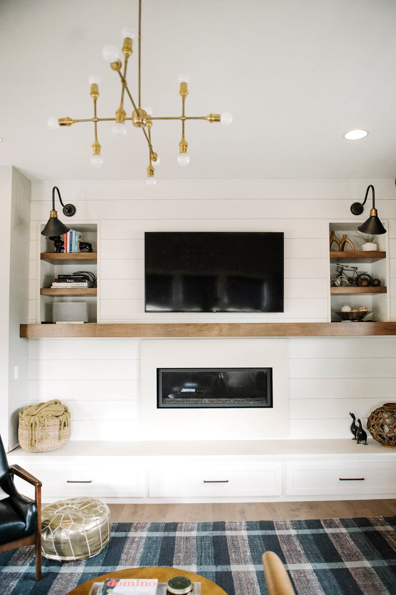 White farmhouse fireplace with built-in bench, shiplap wall, shelves, chandelier.