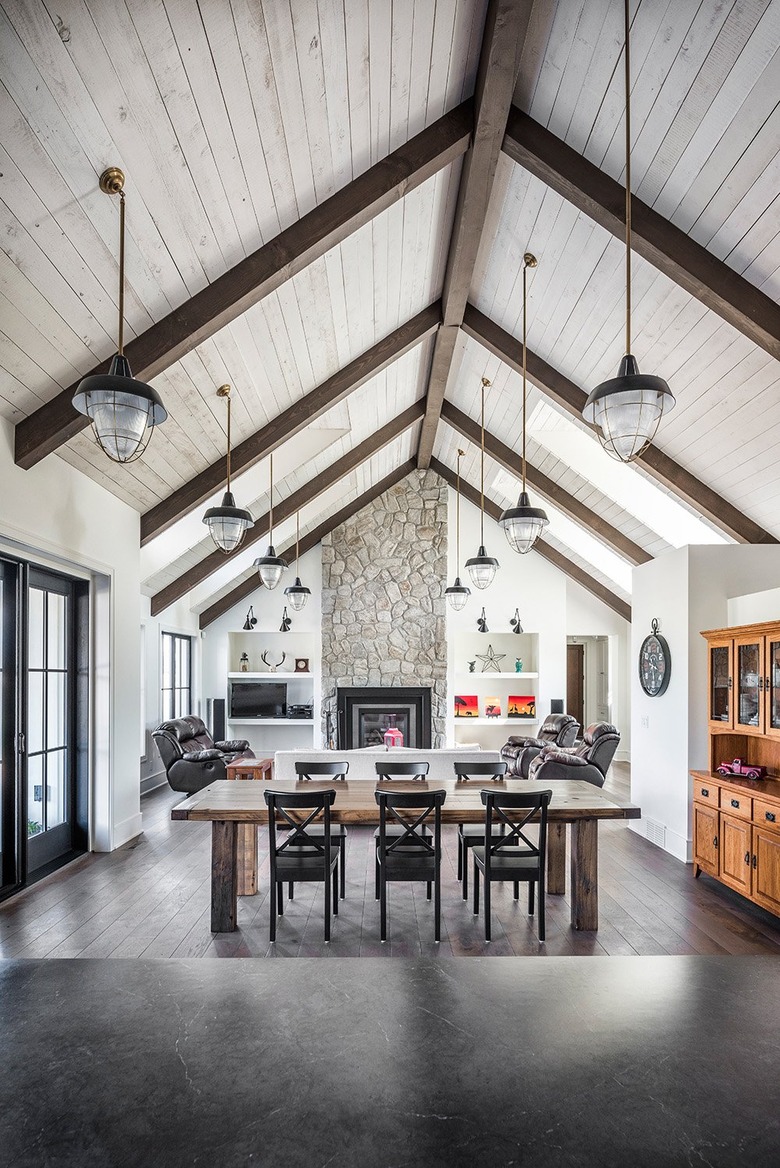 Farmhouse great room with wood beams, stone fireplace, dining table, dark wood floors.