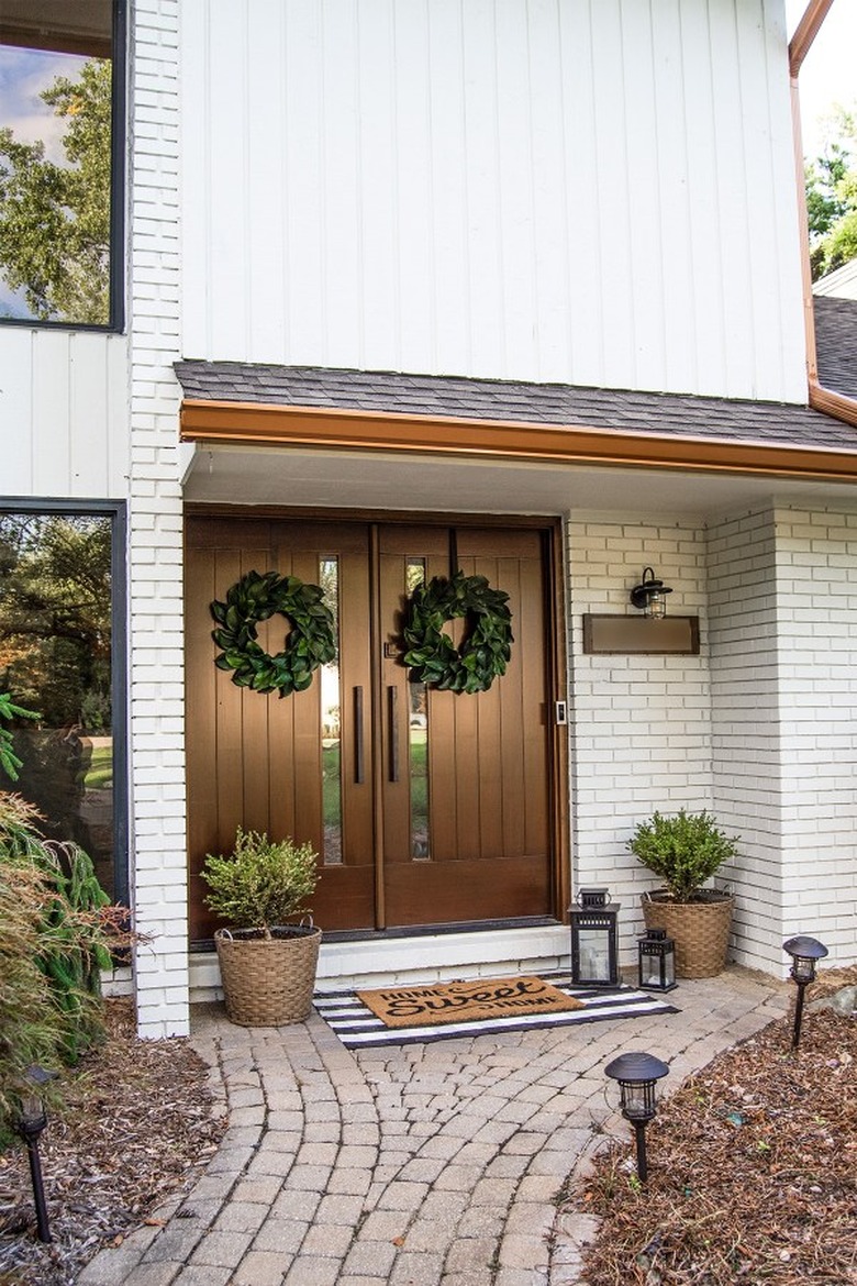 Farmhouse front door idea in a dark wood finish with white brick and green wreaths