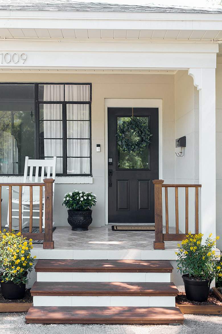 Farmhouse front door idea in black with white exterior and potted plants