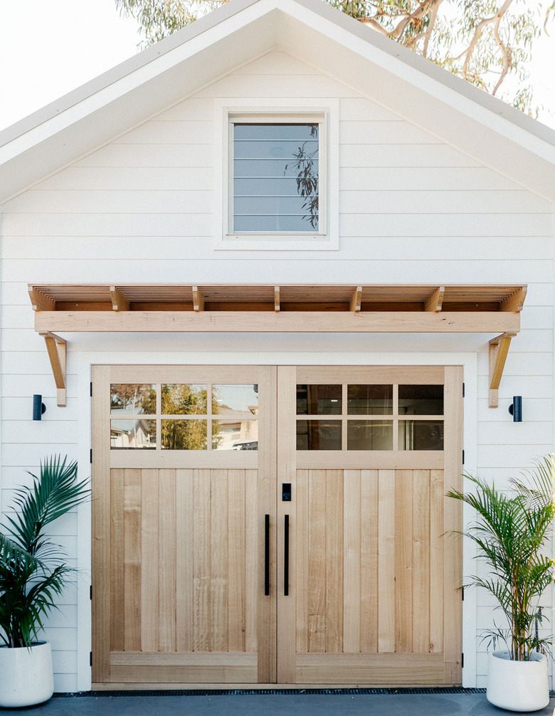 Farmhouse garage doors in wood with wood pergola and white exterior