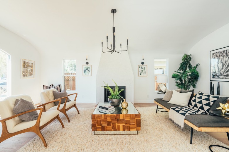 Living room with modernist armchairs, wood and mirrored coffee table, gray upholstered sofa, black industrial chandelier