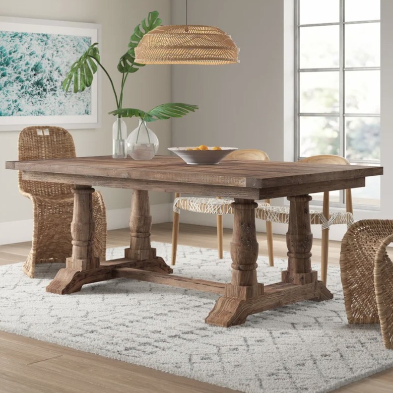 Wood farmhouse table with trestle base, wicker chairs, wicker pendant.