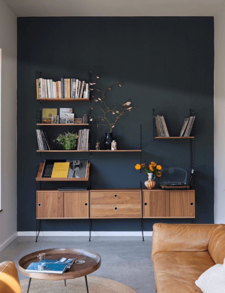 Farrow & Ball's charcoal paint color behind a living room shelving unit stacked with books and vases.