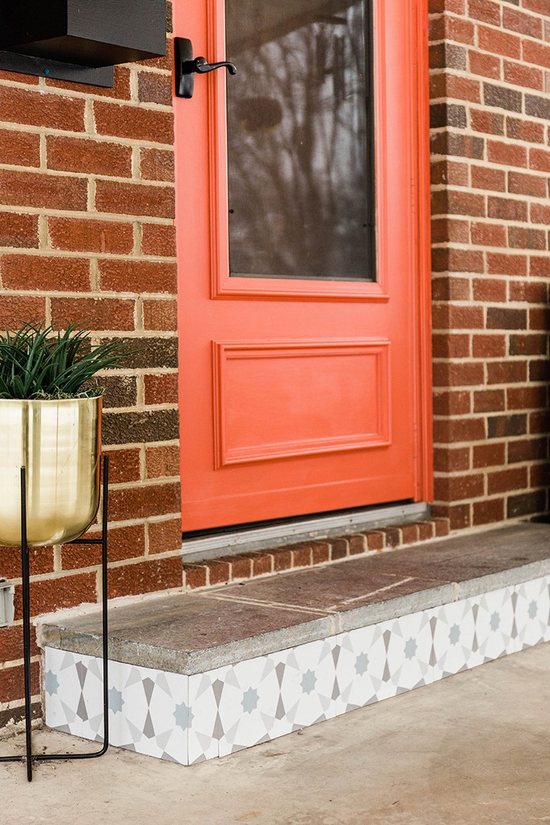 Orange front door of a brick house with a gold plant stand