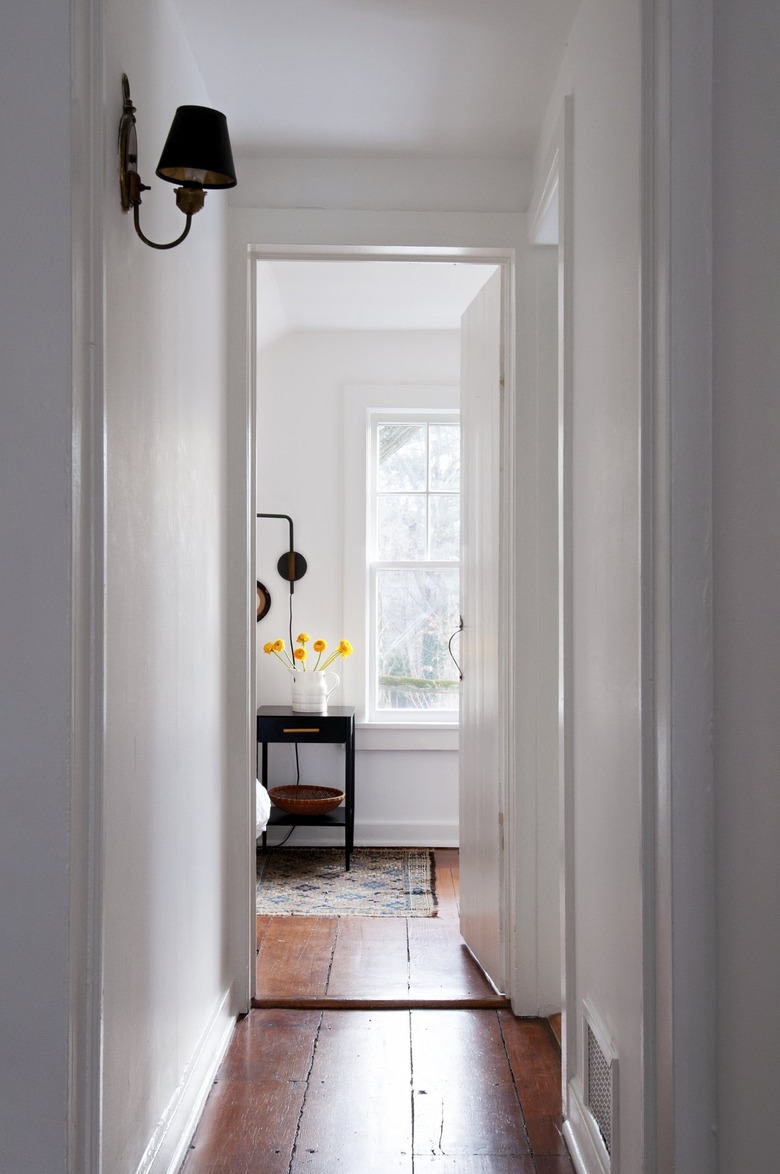 Wood floor hallway with white walls and lamp wall sconce leading to bedroom