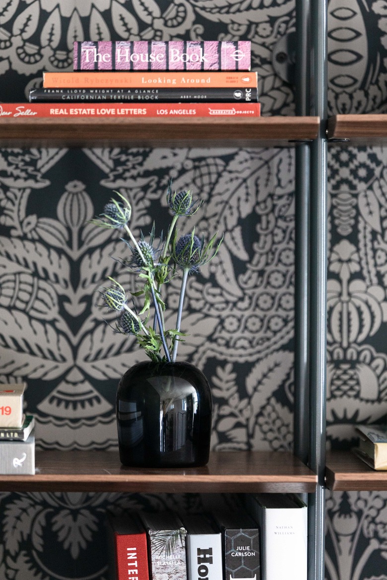 Dark printed wallpaper behind bookshelf with black vase.