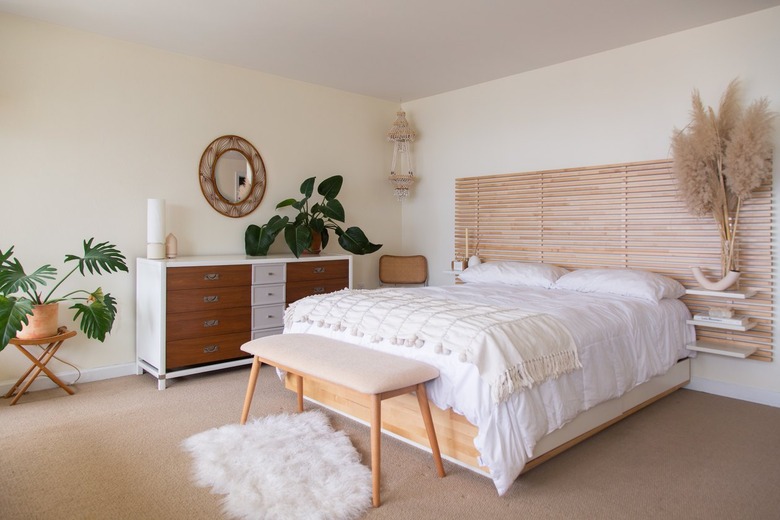 Minimalist bedroom with Boho accents, plants, wood slat headboard, sheepskin rug, wood furniture, beige-white theme.