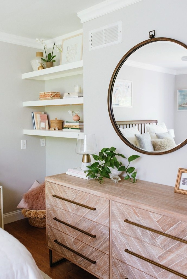 Bedroom shelving idea with modern wood dresser and large round mirror