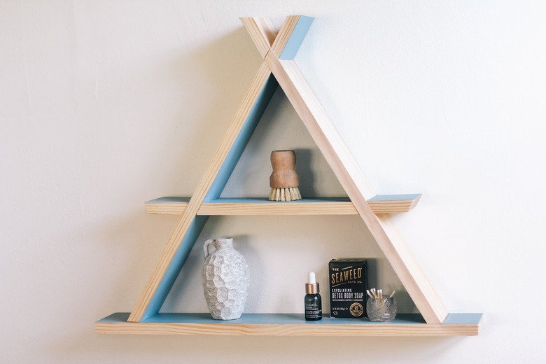 Wooden a-frame shelf with blue inner walls holding small containers on white wall