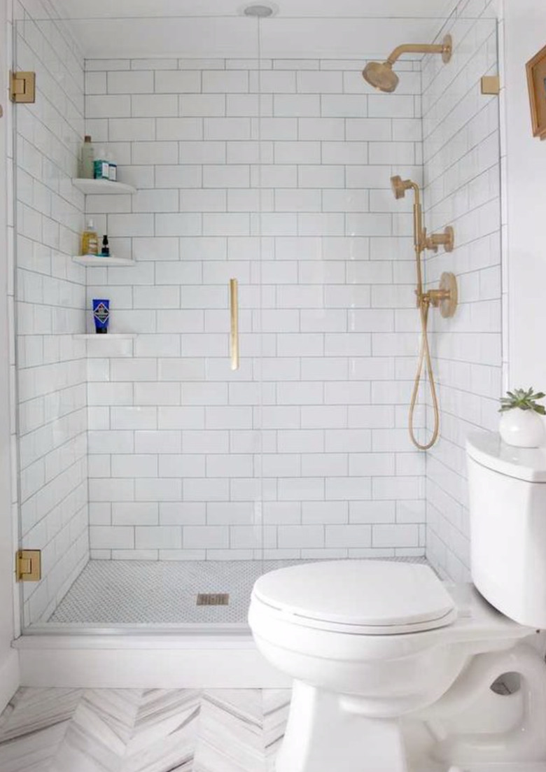 Brass hardware in shower with frameless door and white tile.