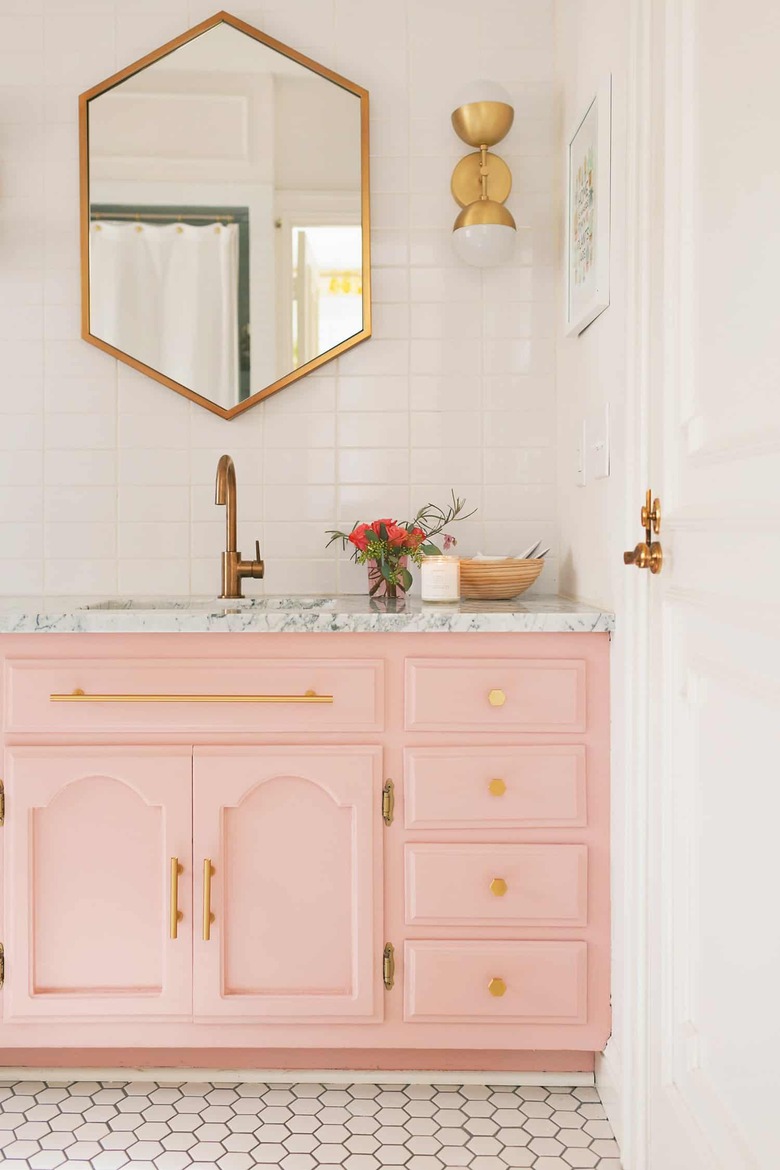 French country bathroom sink in bathroom with pink vanity, marble sink and counter, brass faucets, mirror and light.