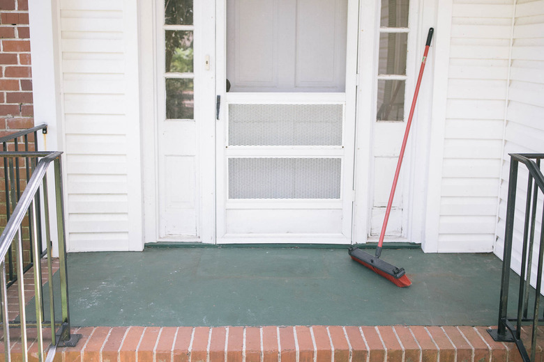 A concrete patio with a white front door; a broom is placed on the front porch