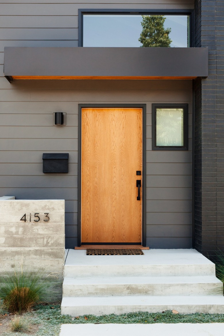 A dark gray house with black accents and a light wood front door. Varied windows and concrete front steps.