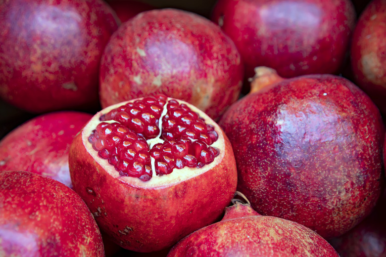 Open fruit of ripe pomegranate with burgundy grains close-up in a pile of pomegranates