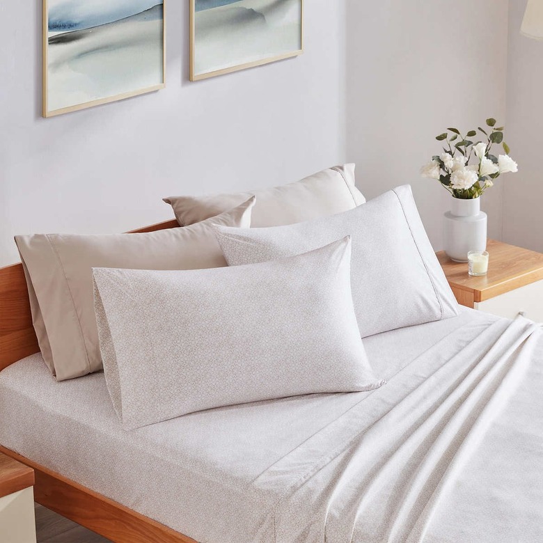 Cream sheets on a bamboo bed with flowers on the bedside table.