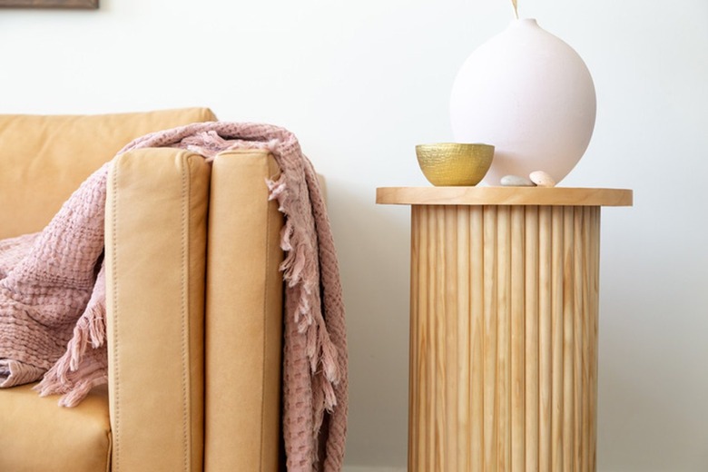 Fluted side table with dowel base, birch circle board tabletop, round pink vase and gold bowl, neutral sofa and pink blanket