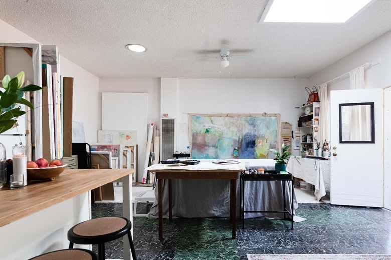 Garage Ideas in Artist gallery with white walls, with large painting attached to one wall, next to shelves with painting supplies and small kitchen island with brown stools