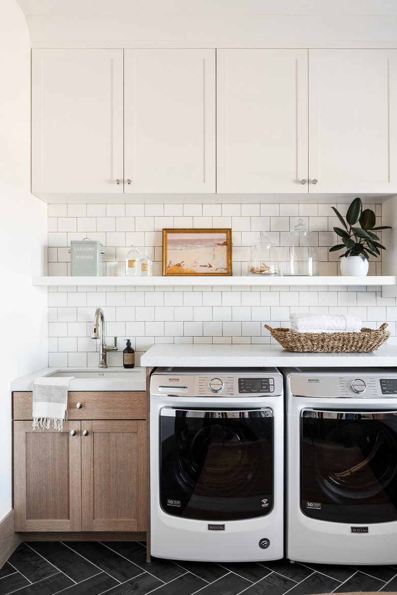 Garage Laundry Room with Front load washer dryer, cupboards, subway tile, white shelf, white cupboard, natural wood sink area.