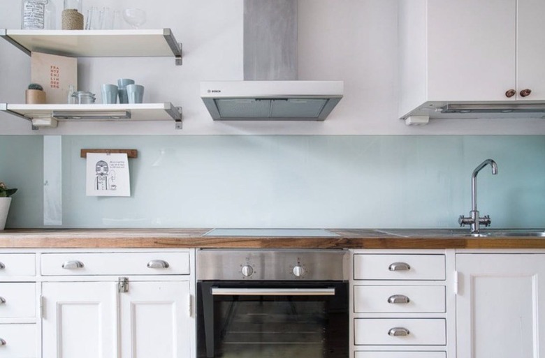 Clear glass backsplash, white cabinets, wood counters, stainless glass top electric stove.