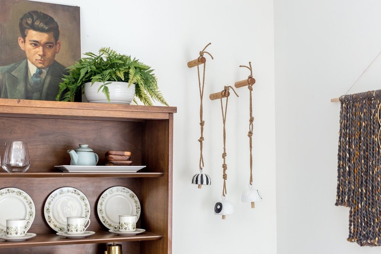 Clay bell wall hanging with wood china cabinet, plant, and art