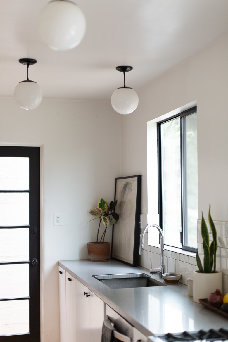 Globe pendant lights, in a kitchen with a gray counter and houseplants.