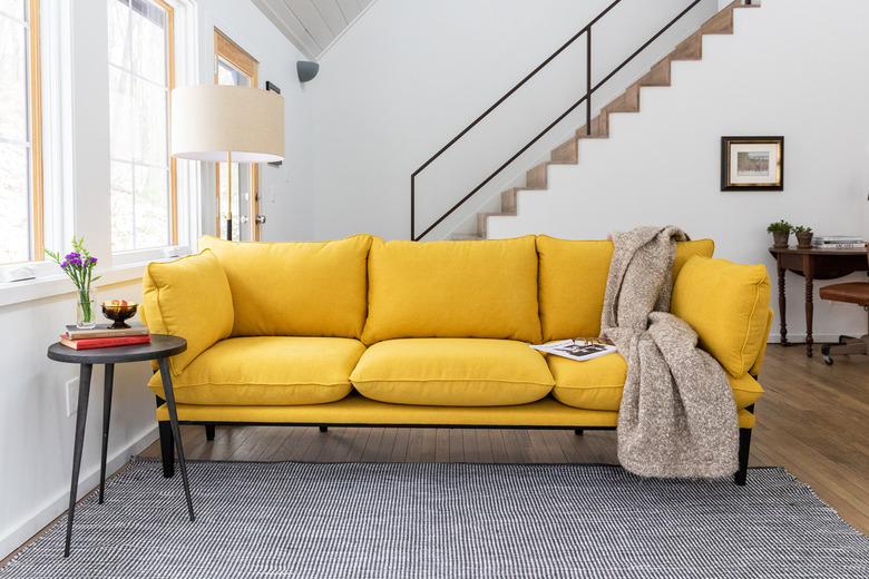 yellow couch near stairs with gray rug and side table