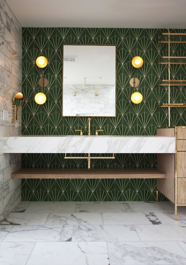 Bathroom with marble vanity, marble floors, green patterned tile wall, brass faucet, sconces, mirror.