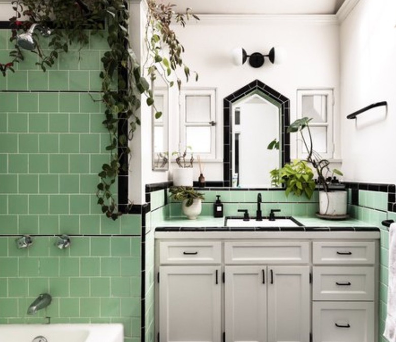 Bathroom with green tiles, black tiles, vanity, plants.