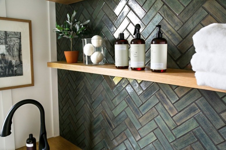 Bathroom with matte green tile backsplash, open shelf, black faucet.