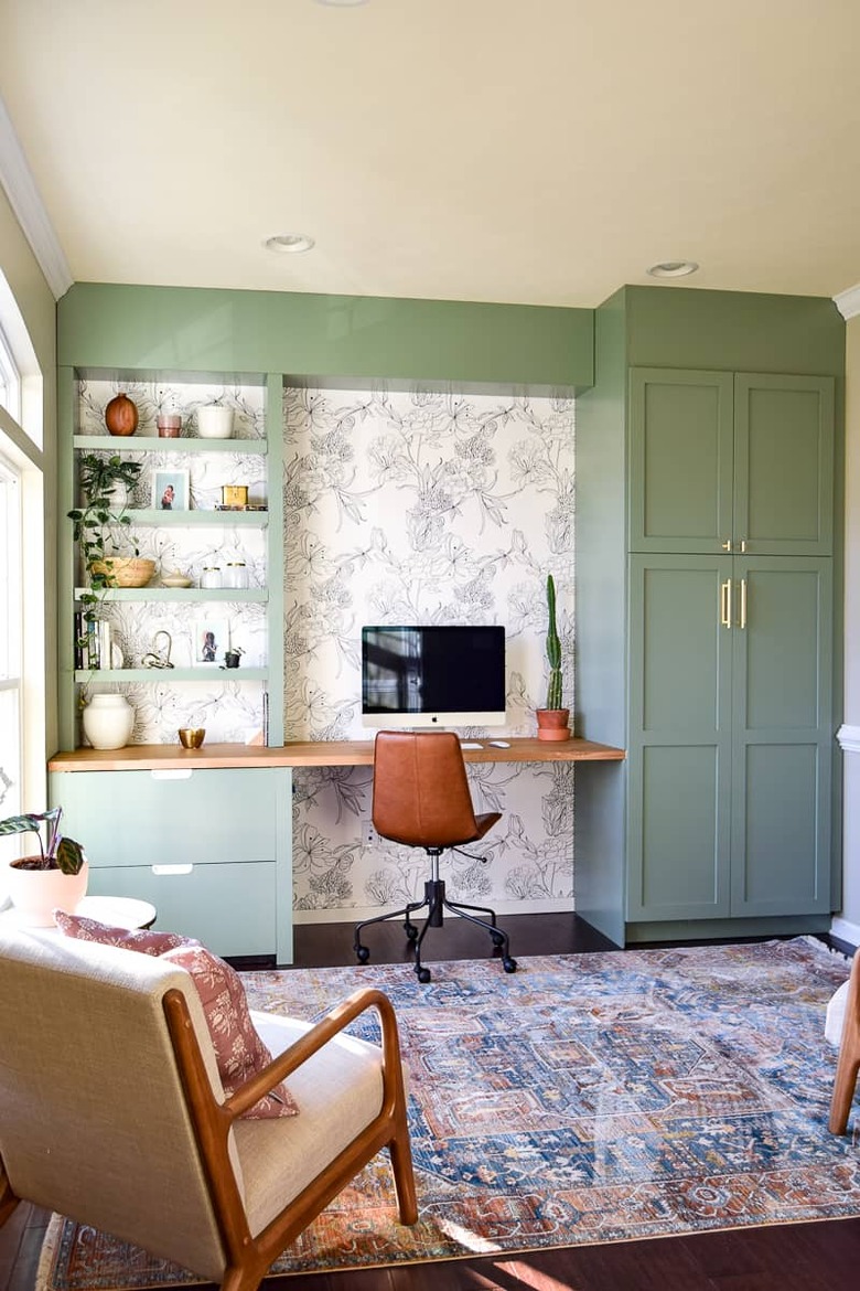 Green home office with green built-ins and black and white wallpaper