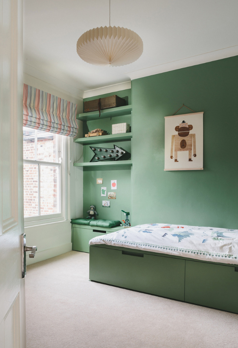 green kids bedroom idea with green wall, shelving, bed and striped Roman shade at window