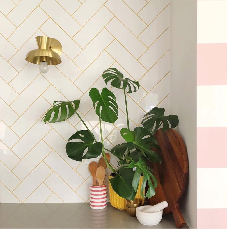 Kitchen backsplash with white subway tile, yellow grout, plant, sconce.