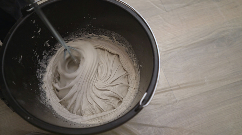 Mixing plaster solution in a bucket, using an electric drill. Mixing beige putty in a bucket using a mixer